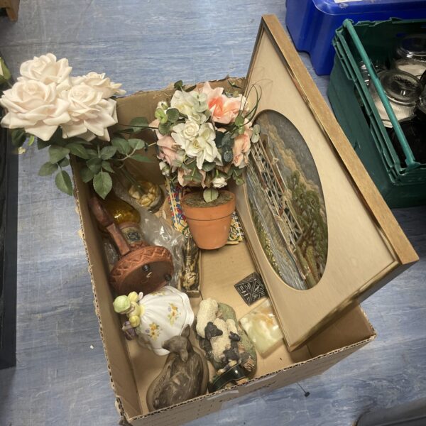 Vintage artificial plant arrangement with framed needlework decor.