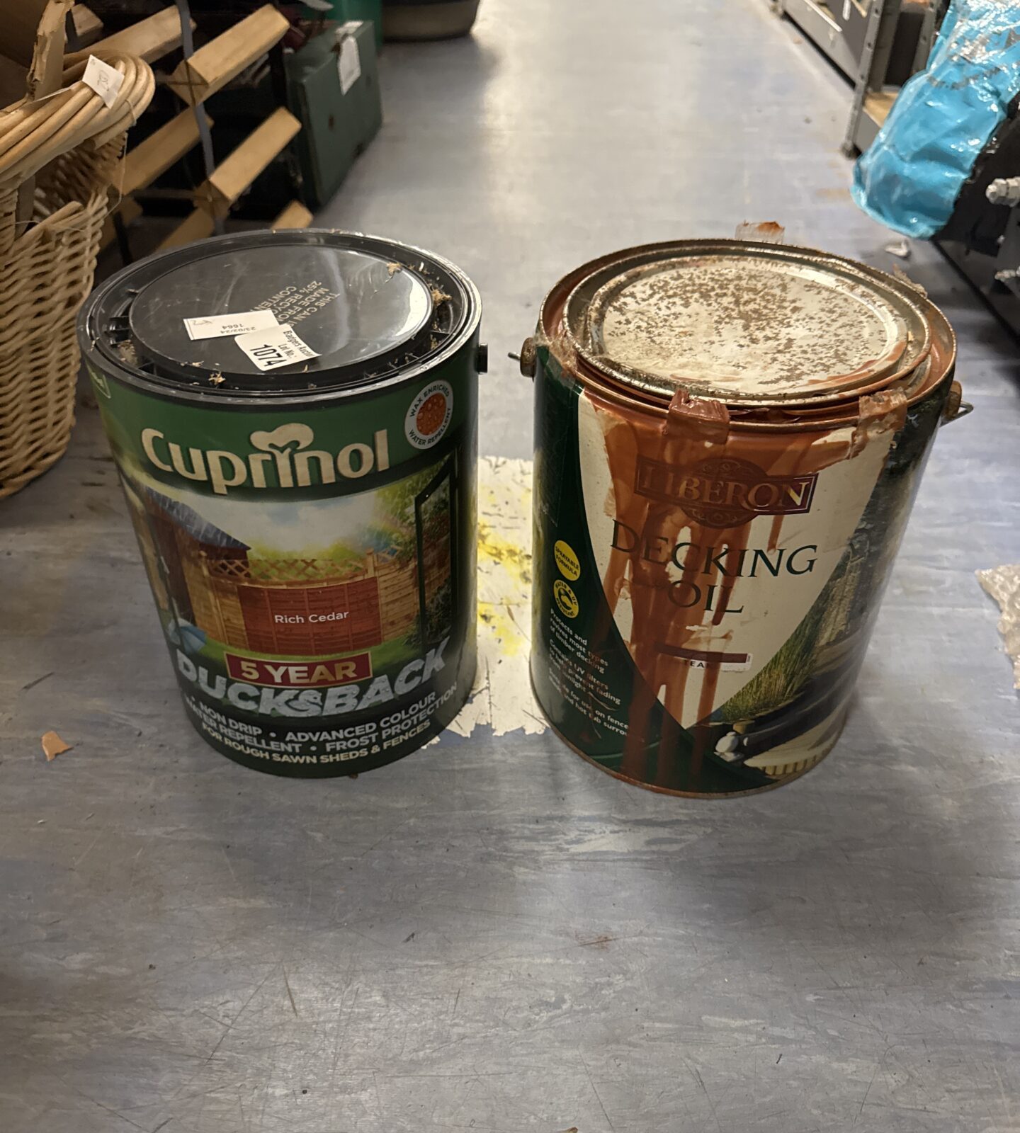 Two tins of decking/fence paint (can on left feels full, one on right 1/3 full)