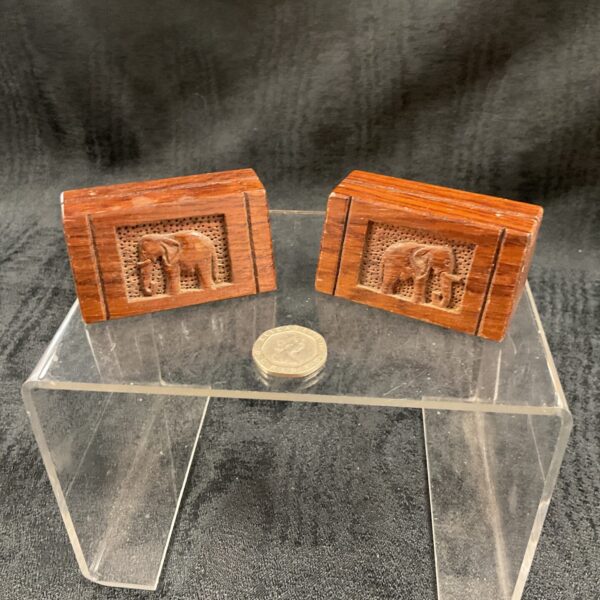 Two hand-carved wooden paper holders with elephant designs on a clear stand.