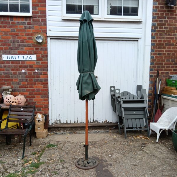 Large green garden parasol with a cast iron base in a garden.