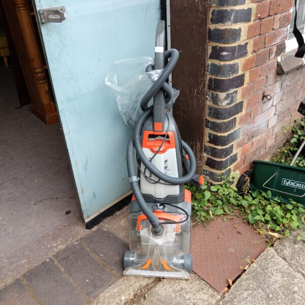 Vax Rapide Ultra carpet cleaner shown against a brick wall.