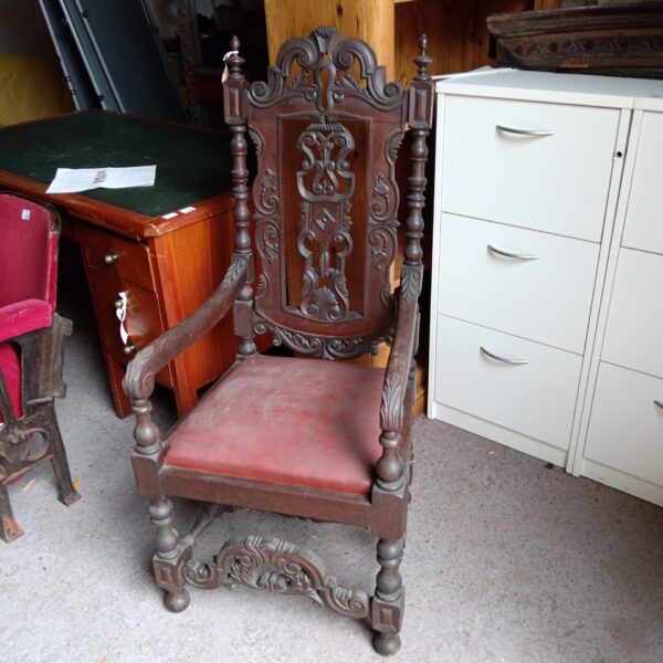 Intricately carved antique oak armchair with worn upholstery.