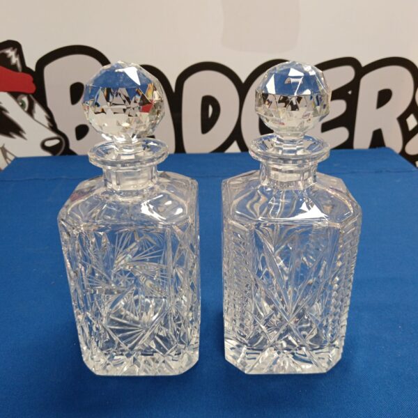 Two elegant crystal whisky decanters with faceted designs.