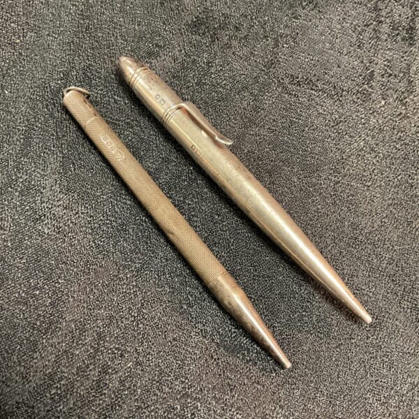 Pair of antique hallmarked silver pencils on a dark surface.
