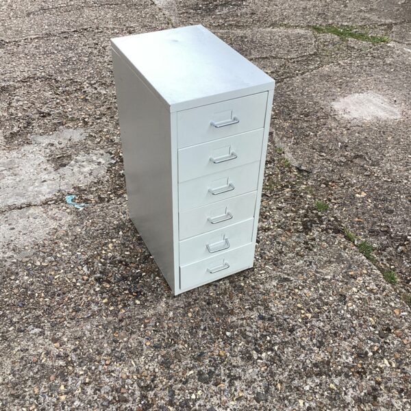 Side view of a small metal drawer unit on a gravel surface.