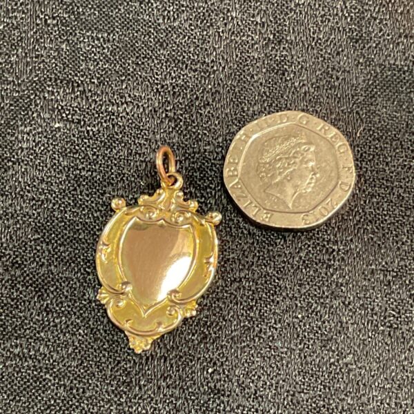 Vintage 9ct gold shield watch fob on a dark surface.