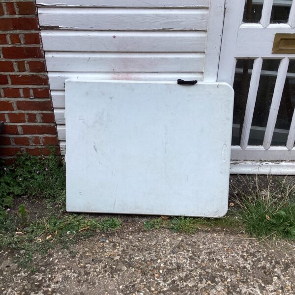 White plastic folding table shown outdoors against a wooden wall.