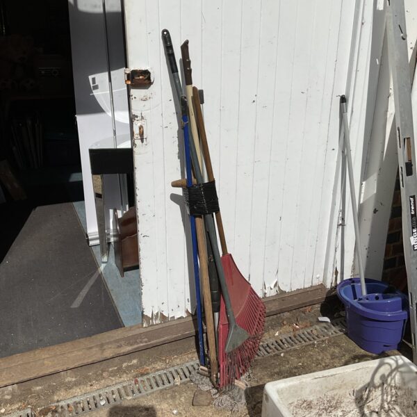 Garden tool bundle featuring a rake and broom leaning against a wall.