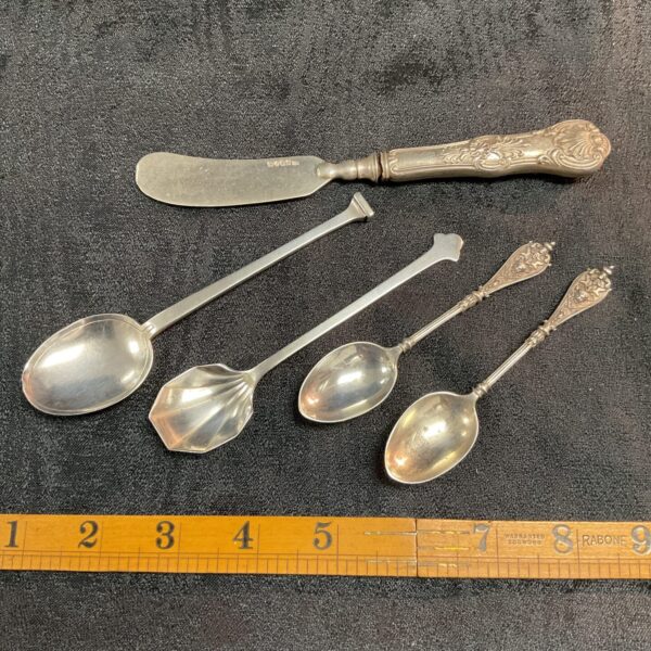 Antique silver spoons and butter knife on ruler.