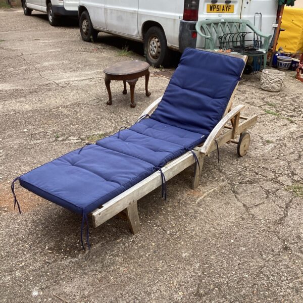 Vintage teak sun lounger with blue cushion in a garden setting.