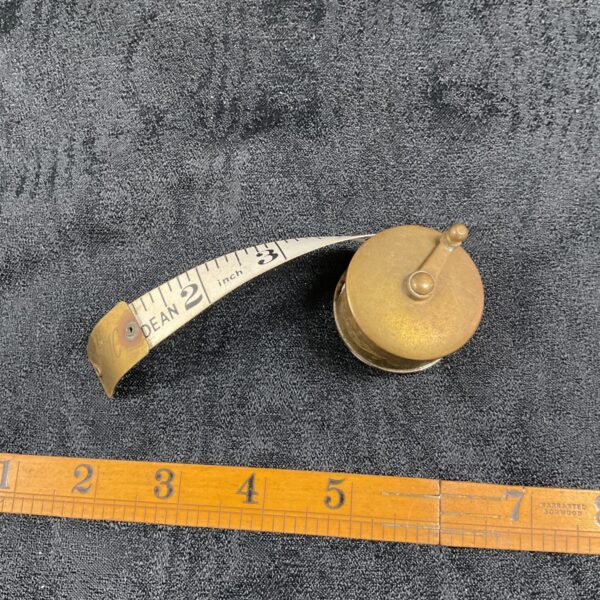 Close-up of vintage brass reel tape measure with extended tape.