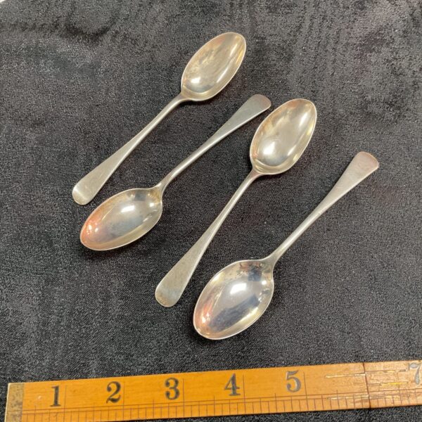 Antique silver teaspoons displayed on a dark surface.