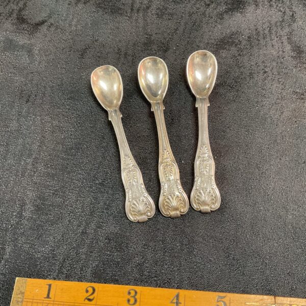 Three Georgian silver teaspoons in the Kings pattern displayed on a dark surface.