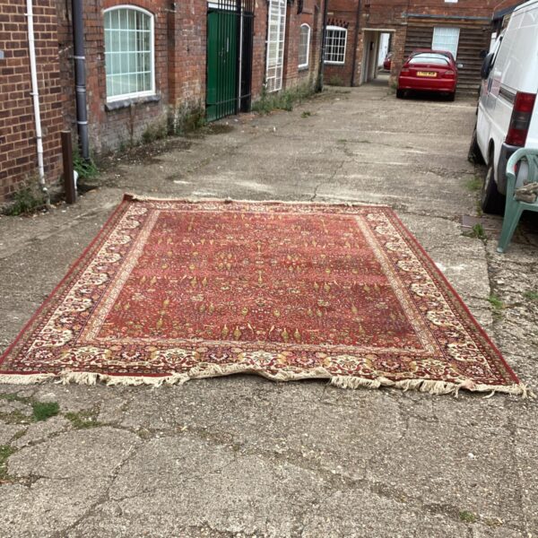 Vintage Persian rug displayed outdoors on a gravel surface.