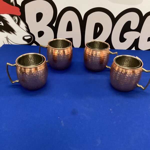 Set of four hammered copper coffee cups on a blue background.