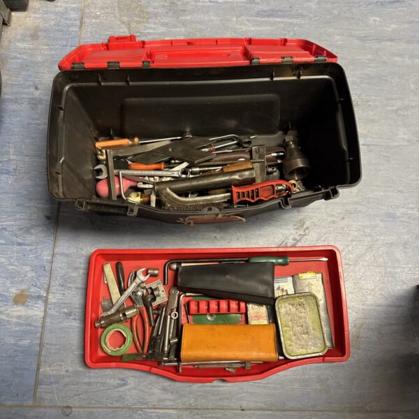 Red plastic toolbox filled with assorted hand tools for workshop storage.
