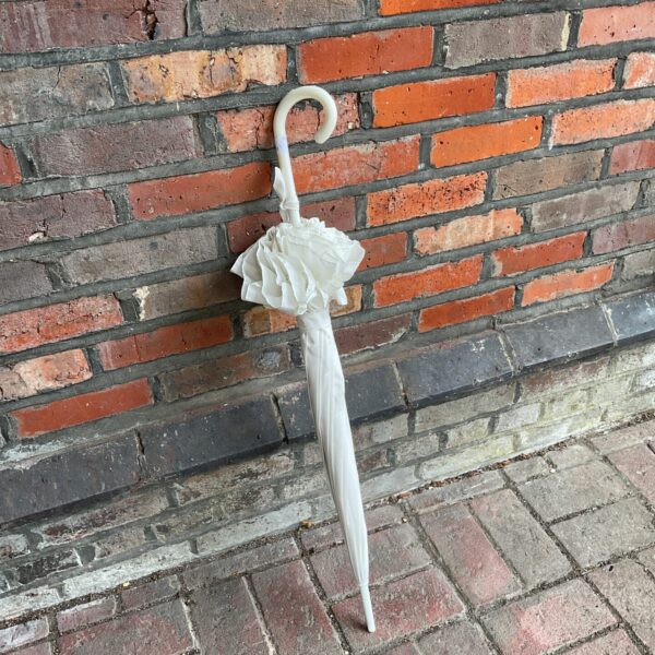Vintage white ruffled umbrella leaning against a brick wall.