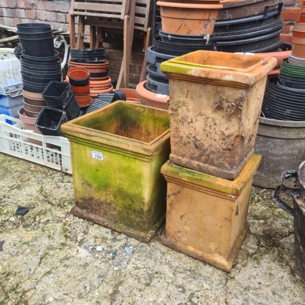 Square terracotta planters in a garden setting, ideal for plants.