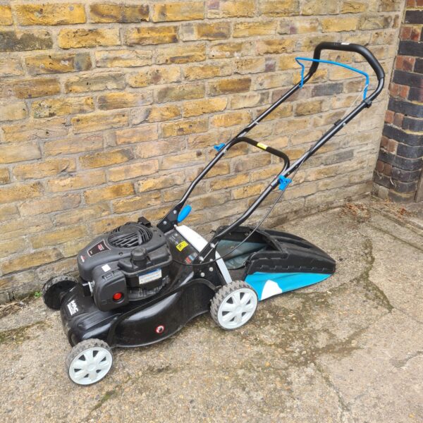 MacAllister petrol lawnmower standing against a brick wall.