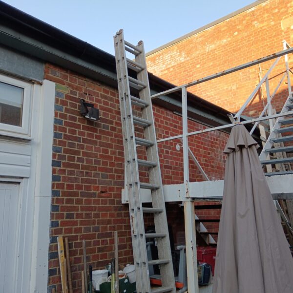 Large aluminium builders ladder reaching towards a brick wall.