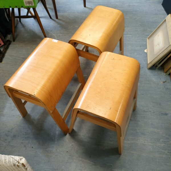 Three vintage bentwood stools with curved seats and angled legs.