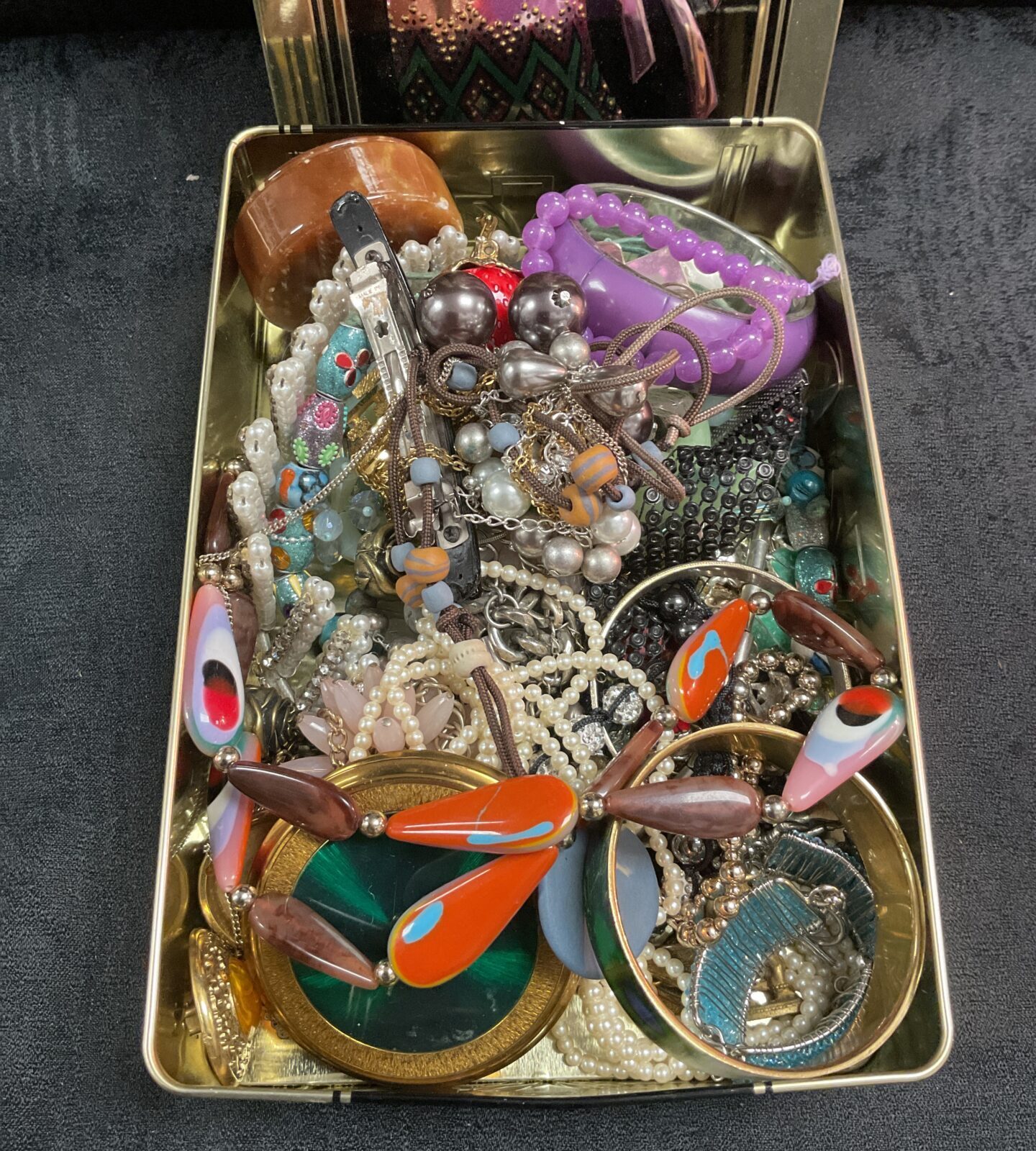 Vintage costume jewellery lot in a tin, assorted necklaces and brooches.