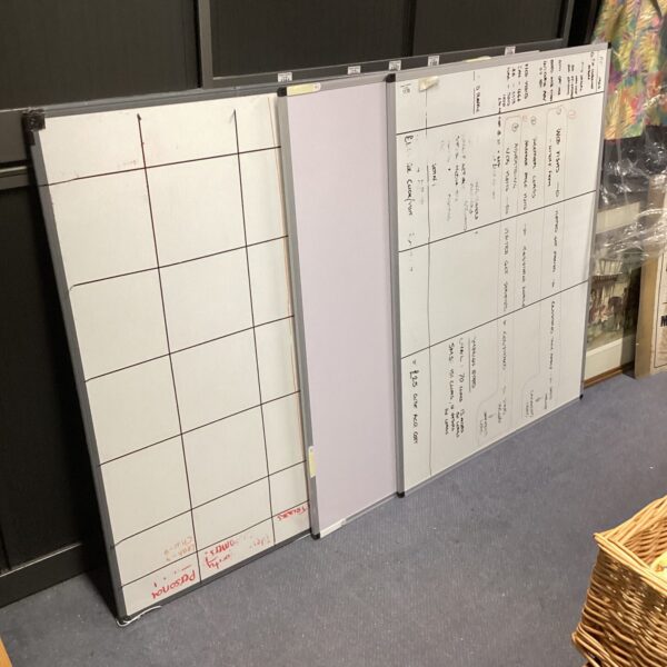 Three large whiteboards stacked against a wall, ready for use.