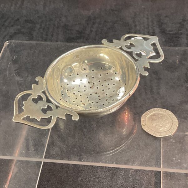 Antique silver tea strainer with pierced bowl and scrolling handles.