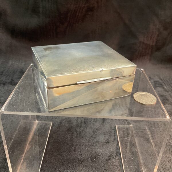 Vintage silver cigarette box on a clear stand.