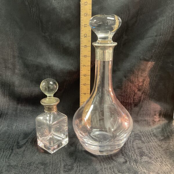 Antique silver collared decanter and bottle set on dark background.
