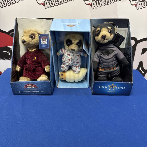 Three meerkat plush toys in a box.