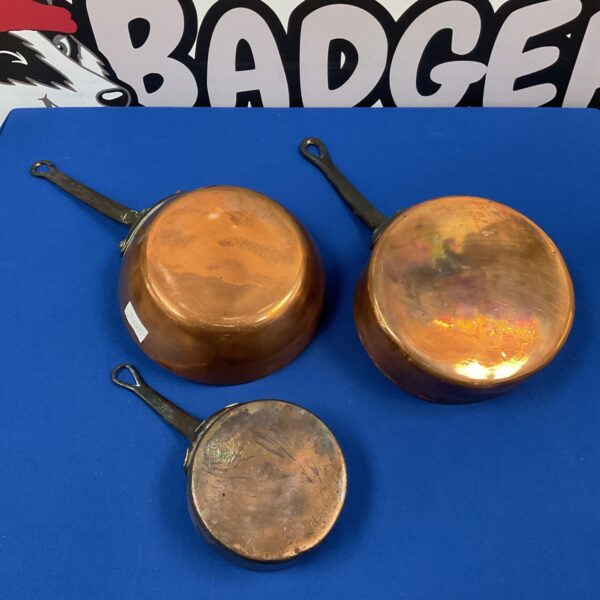 Set of three antique copper pans on a blue background.