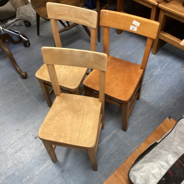 Three vintage wooden children's chairs with a rustic patina.