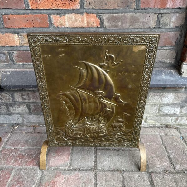 Vintage brass fire screen with detailed ships at sea.