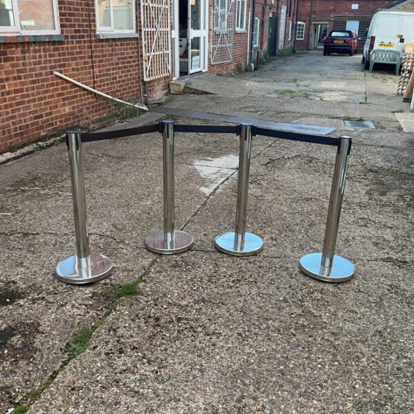 Four chrome barrier posts with retractable belts for queue control.