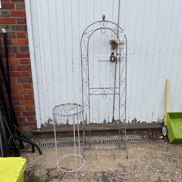 Vintage metal garden trellis and plant stand in a garden setting.