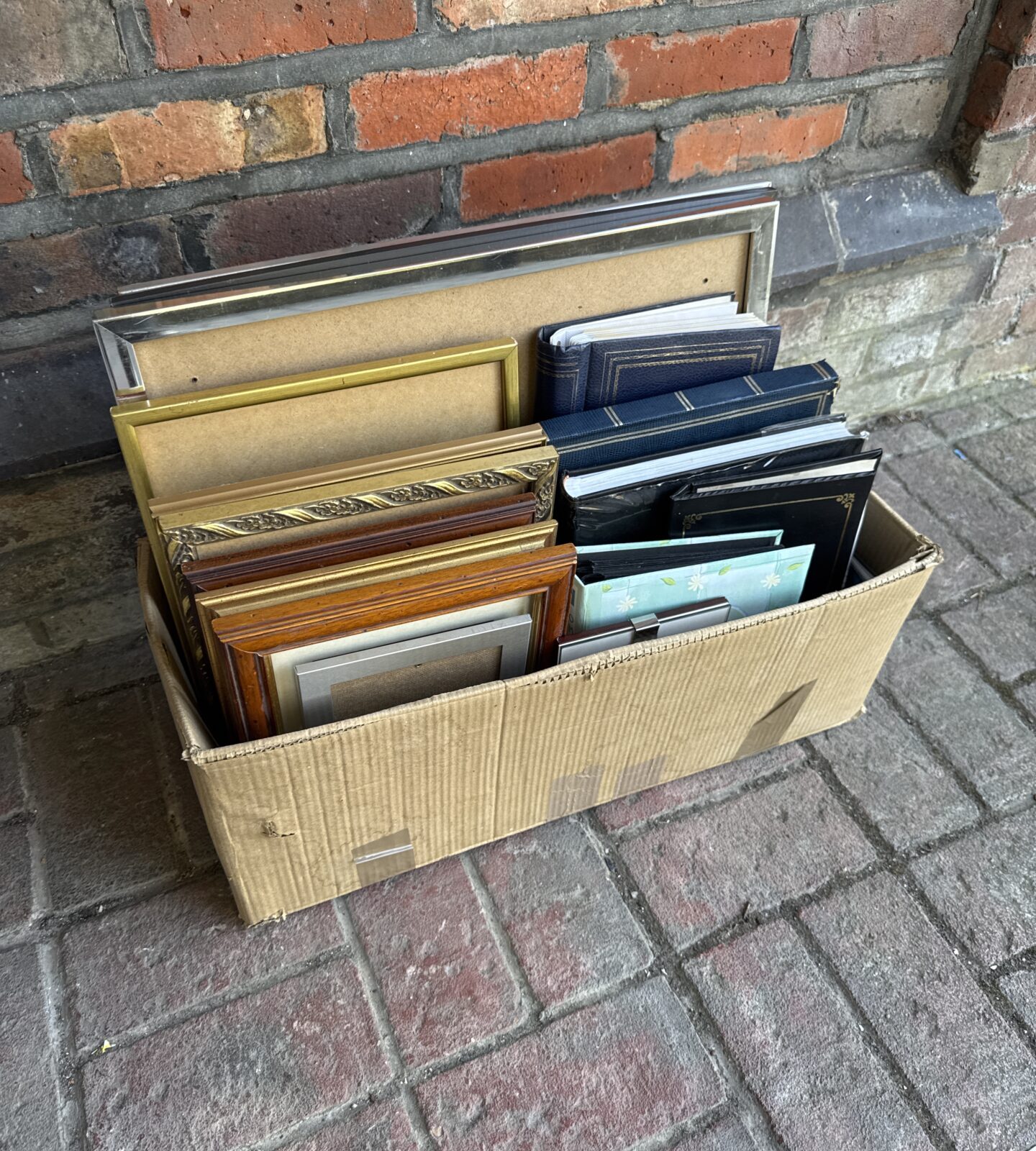 Assorted vintage picture frames and photo albums in a cardboard box.