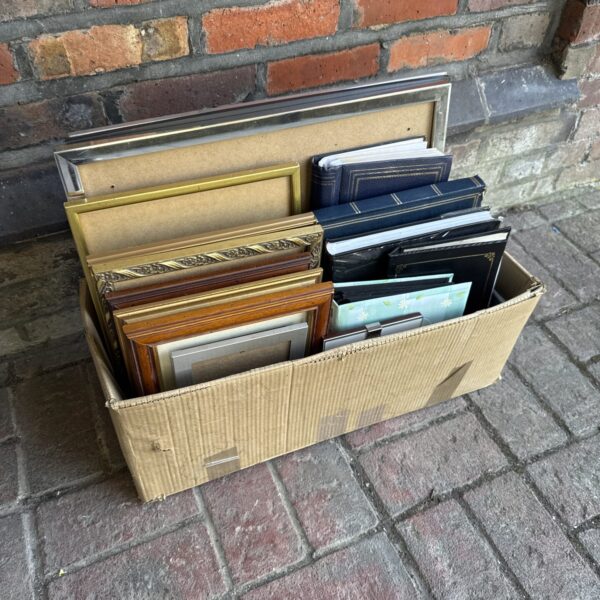 Assorted vintage picture frames and photo albums in a cardboard box.