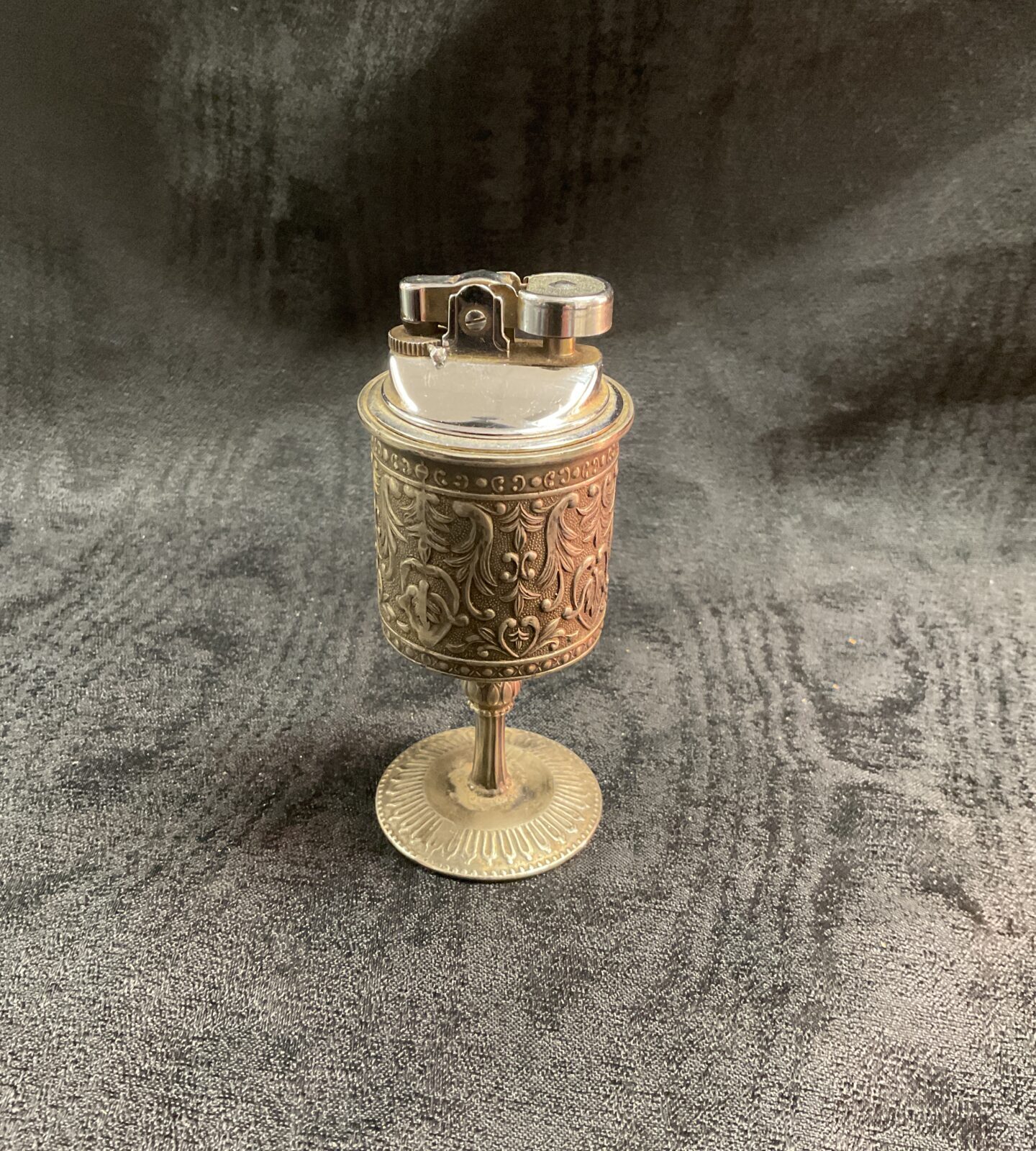 Ornate vintage pedestal gas lighter on a dark surface.