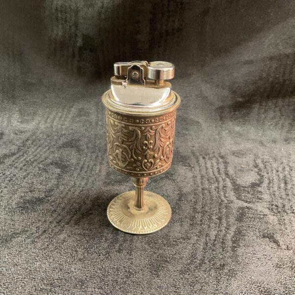Ornate vintage pedestal gas lighter on a dark surface.