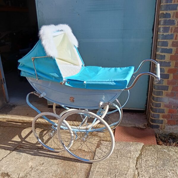 Side view of a vintage silver cross pram with a blue interior.