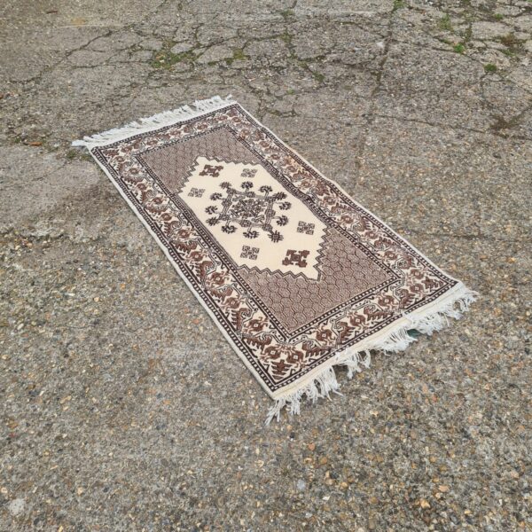 Vintage Tunisian runner rug displayed outdoors on gravel.
