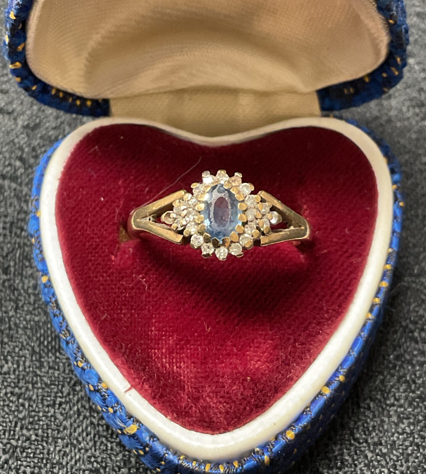 Close-up of a 9ct gold sapphire and diamond cluster ring on velvet.