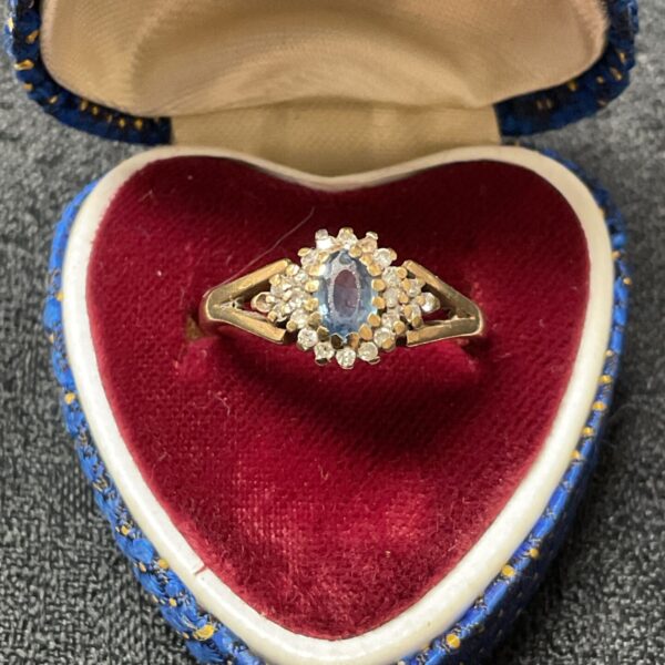 Close-up of a 9ct gold sapphire and diamond cluster ring on velvet.