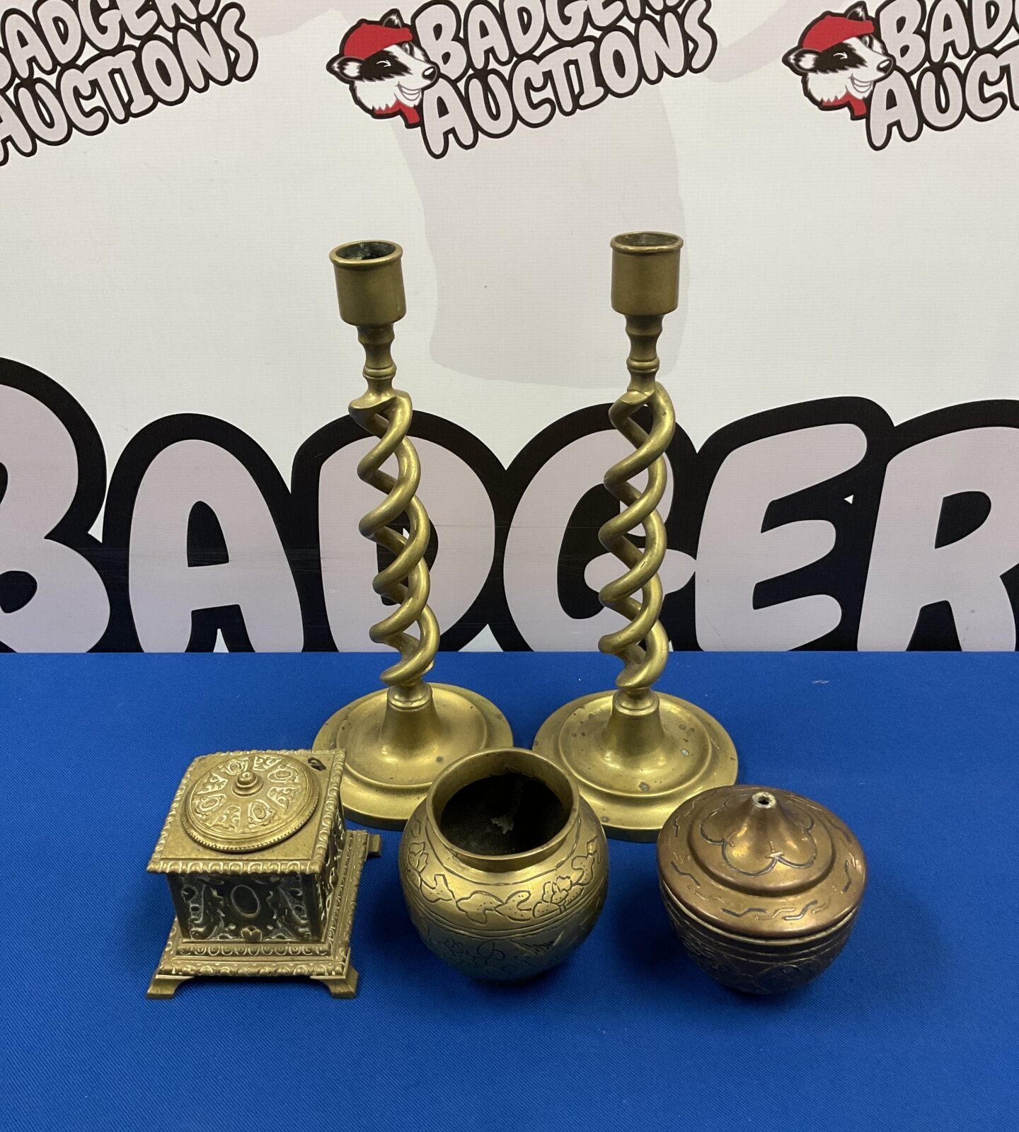 Antique brass candlesticks, tobacco jar, and pot on a blue surface.