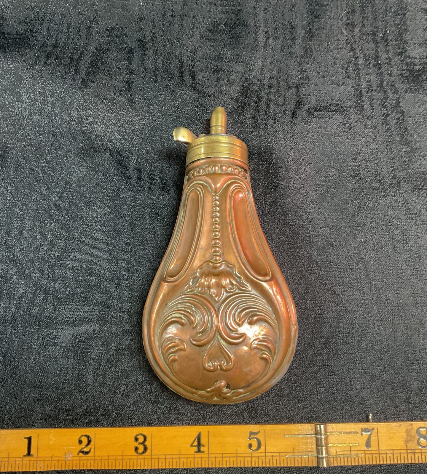 Intricate antique copper powder flask with embossed floral design.