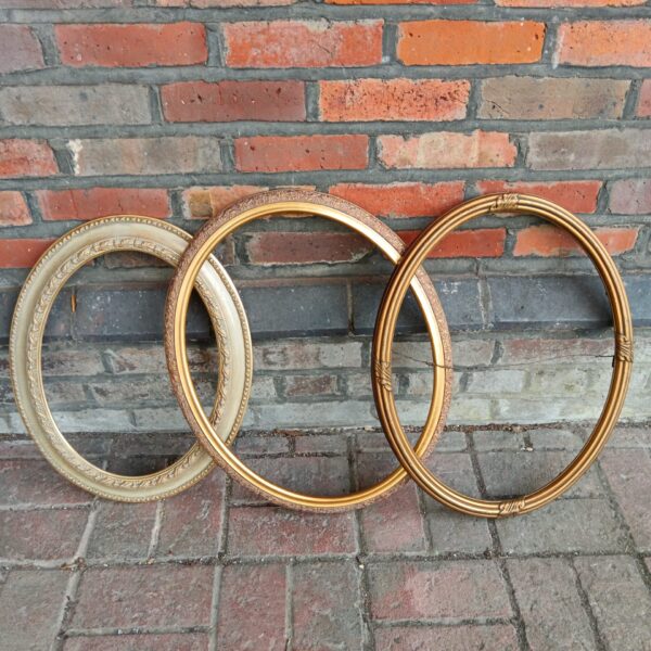 Three antique gilt oval picture frames with ornate detailing.