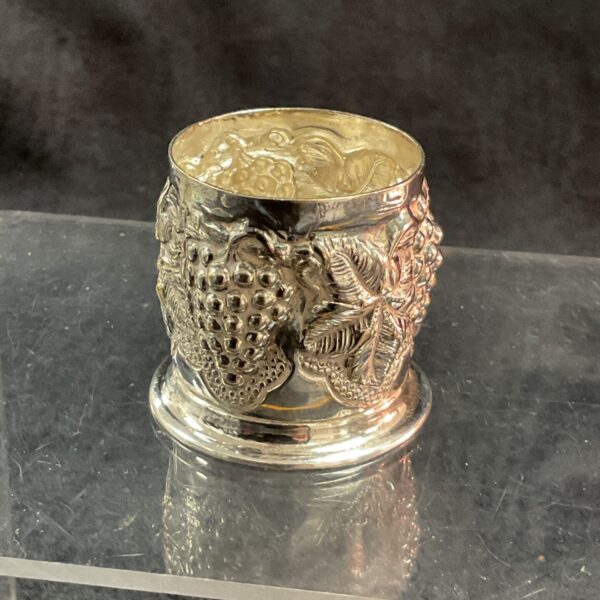 Intricate embossed silver christening cup on reflective surface.