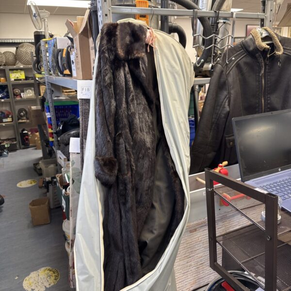 Full length black ebony mink fur coat draped on a rack.