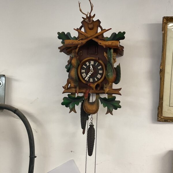 Vintage Black Forest cuckoo clock with detailed hunting scene carvings.